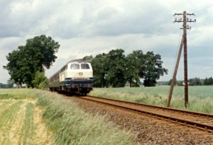 Ein Zug durchfährt bei Xanten eine Landschaft mit Feldern und Bäumen im Hintergrund. Lok ist 215 021